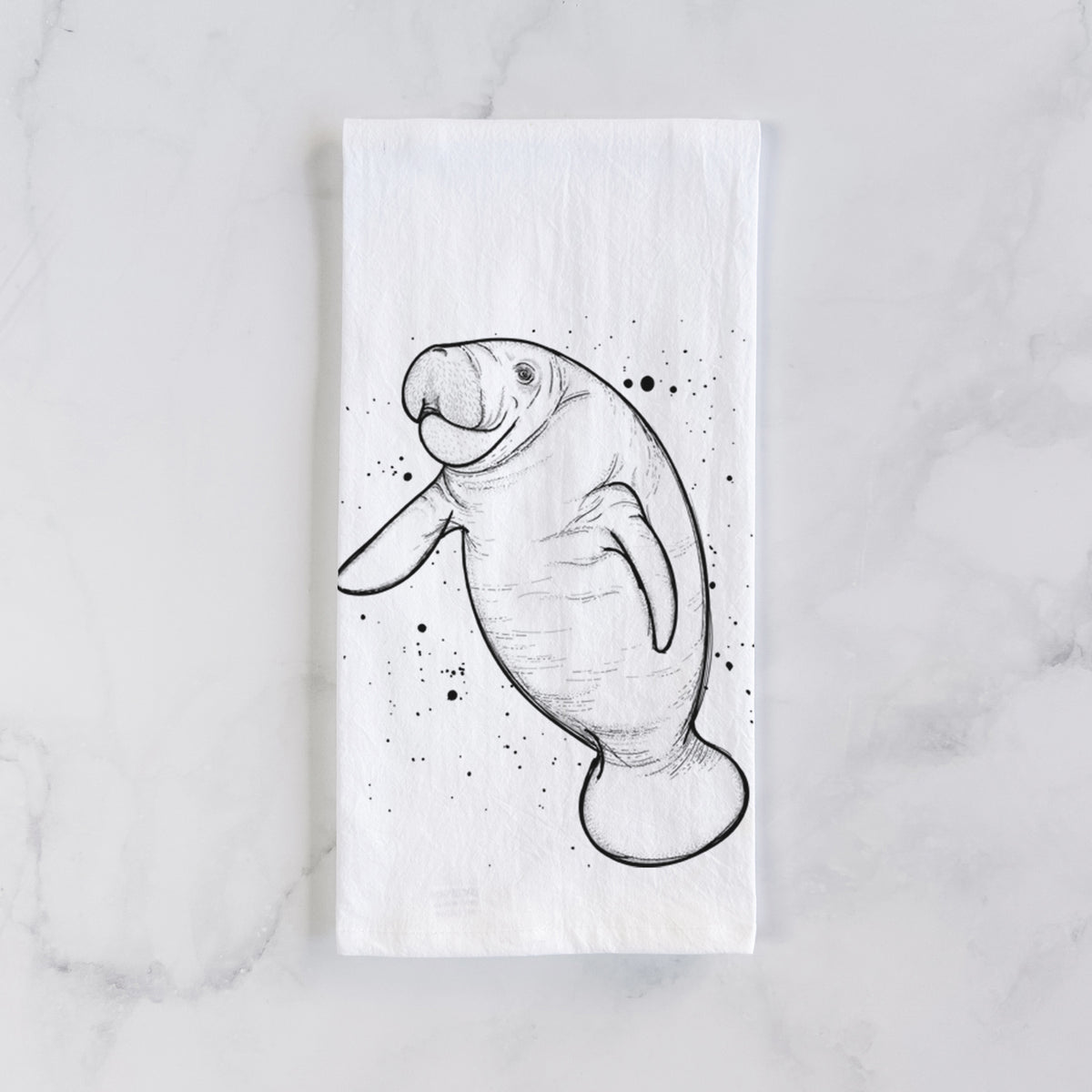 White cotton tea towel laid flat on marble, printed with a black ink line drawing of a manatee swimming, with ink splatters.