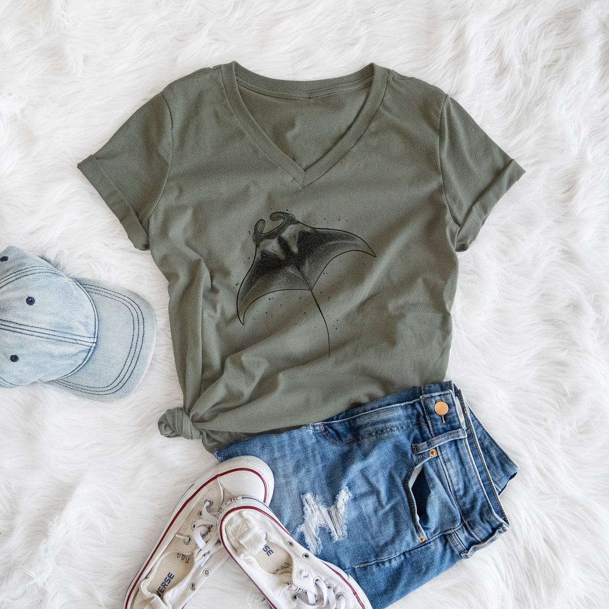 Military green women's relaxed fit cotton V-neck t-shirt printed with a black ink illustration of a manta ray gliding, styled flat on a white faux fur rug with a cap, jeans and sneakers.