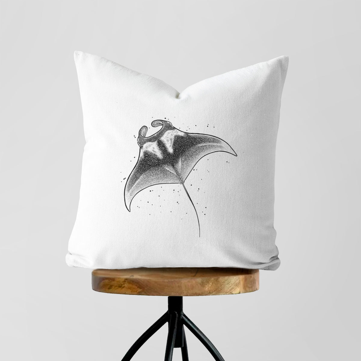 White pillow cover printed with a black ink illustration of a manta ray gliding, on a wooden stool.