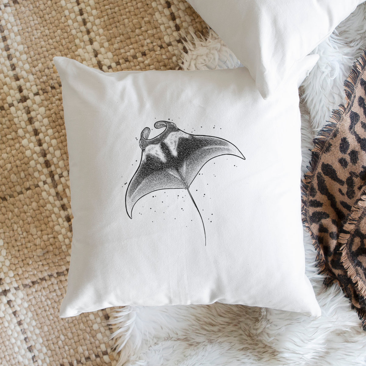 White pillow cover printed with a black ink illustration of a manta ray gliding, on a woven chair.