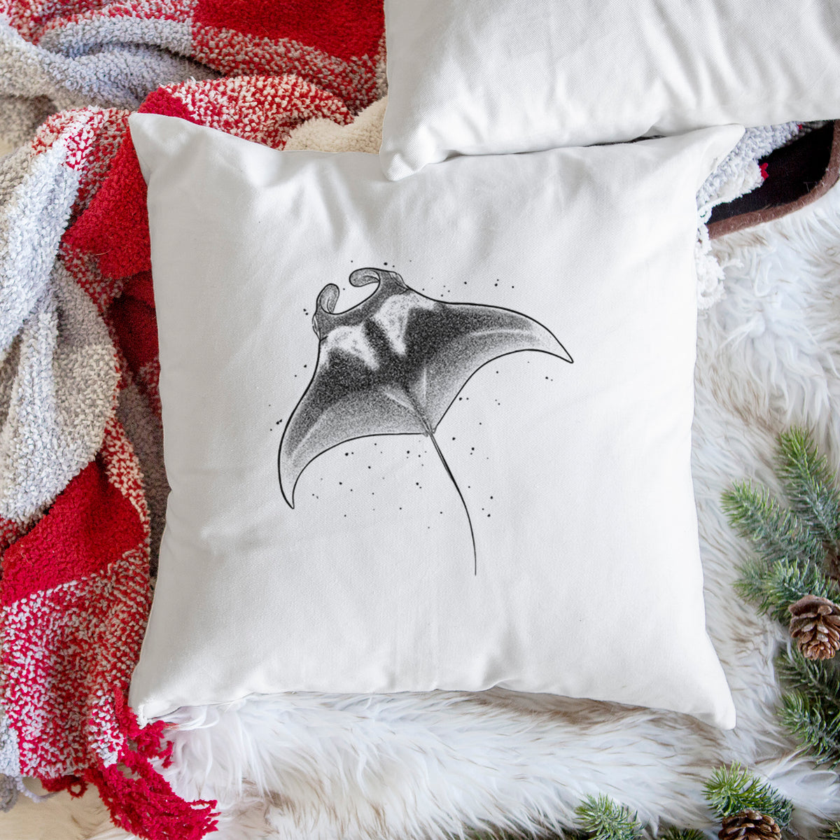 White pillow cover printed with a black ink illustration of a manta ray gliding, on a woven chair.