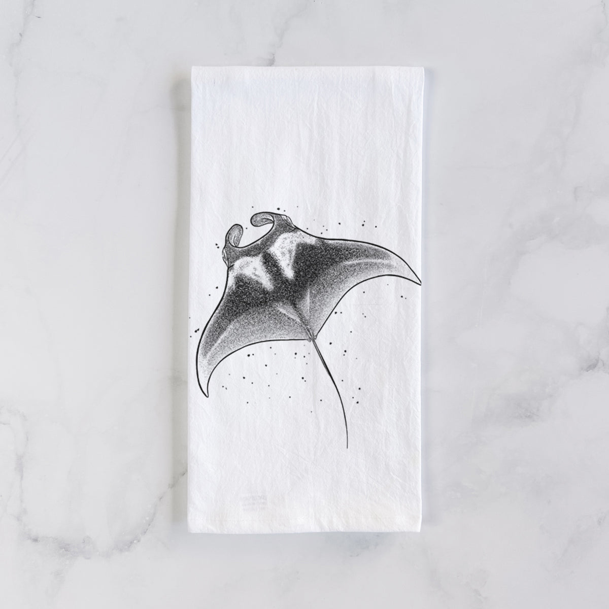 White cotton tea towel laid flat on marble, printed with a black ink illustration of a manta ray gliding.