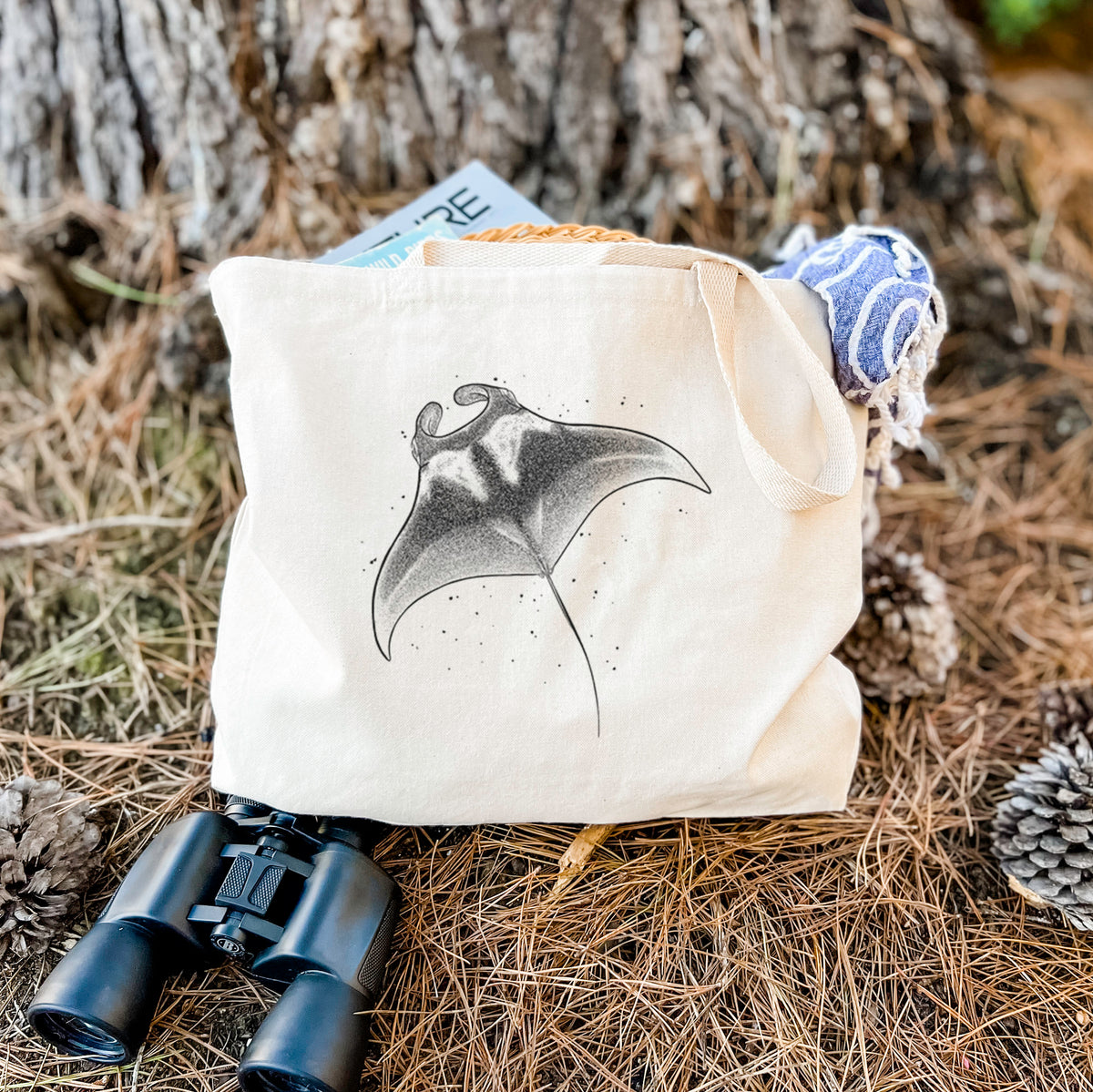 Canvas tote bag printed with a black ink illustration of a manta ray gliding, resting on dry grass beside a pair of binoculars.