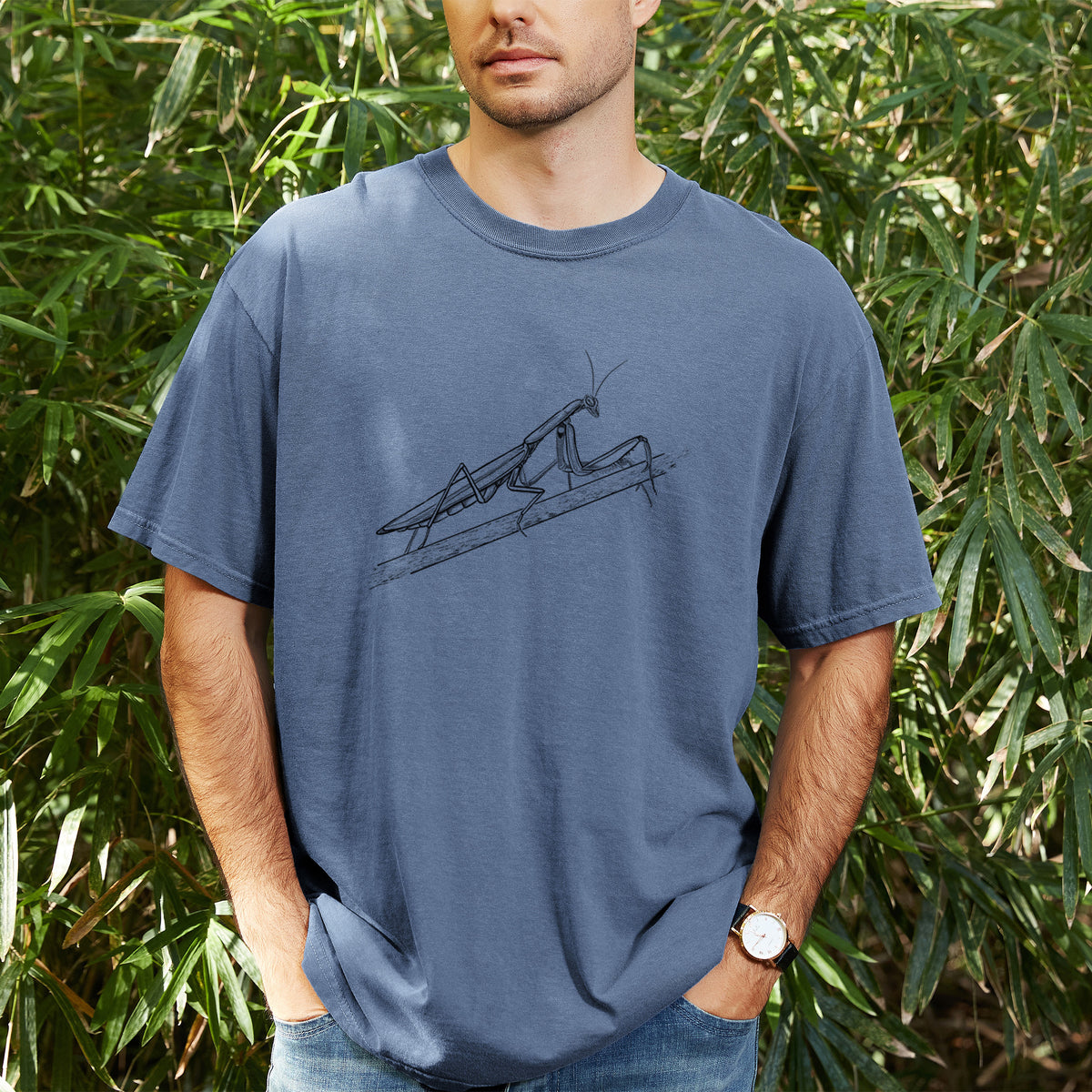 Man wearing a Comfort Colors t-shirt printed with a detailed black ink illustration of a praying mantis on a stem, outdoors.