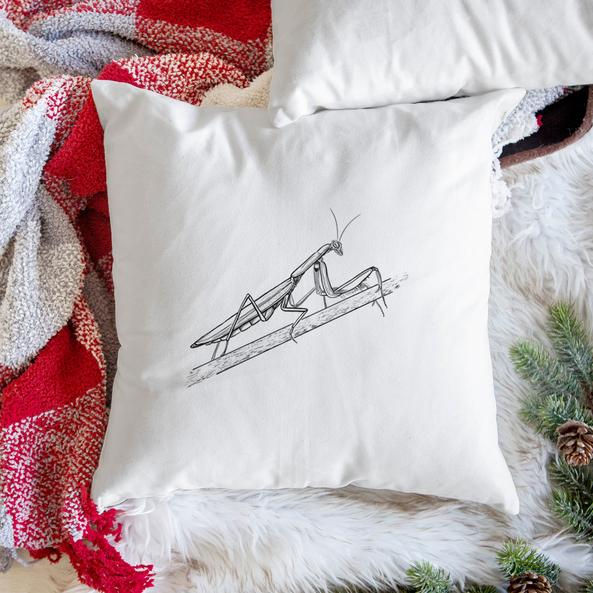 White pillow cover printed with a detailed black ink illustration of a praying mantis on a stem, on a woven chair.