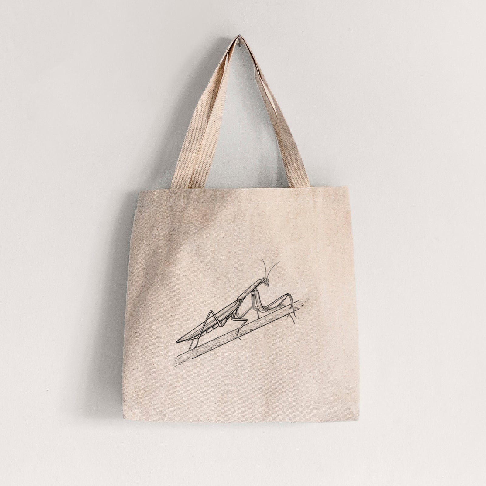 Natural canvas tote bag printed with a detailed black ink illustration of a praying mantis on a stem.
