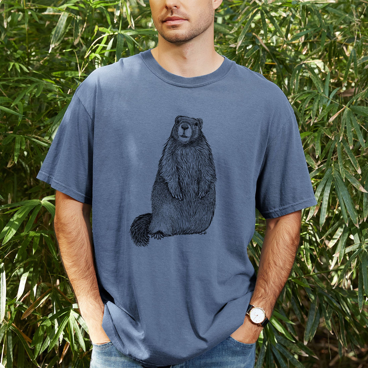 Man wearing a Comfort Colors t-shirt printed with a detailed black ink illustration of a marmot standing upright, outdoors.