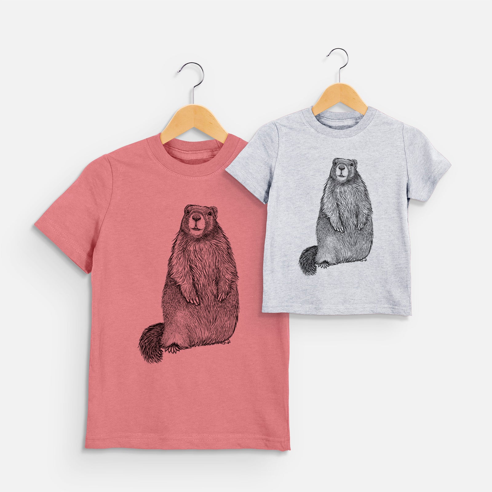 Two youth t-shirts in different colors on hangers, printed with a detailed black ink illustration of a marmot standing upright.