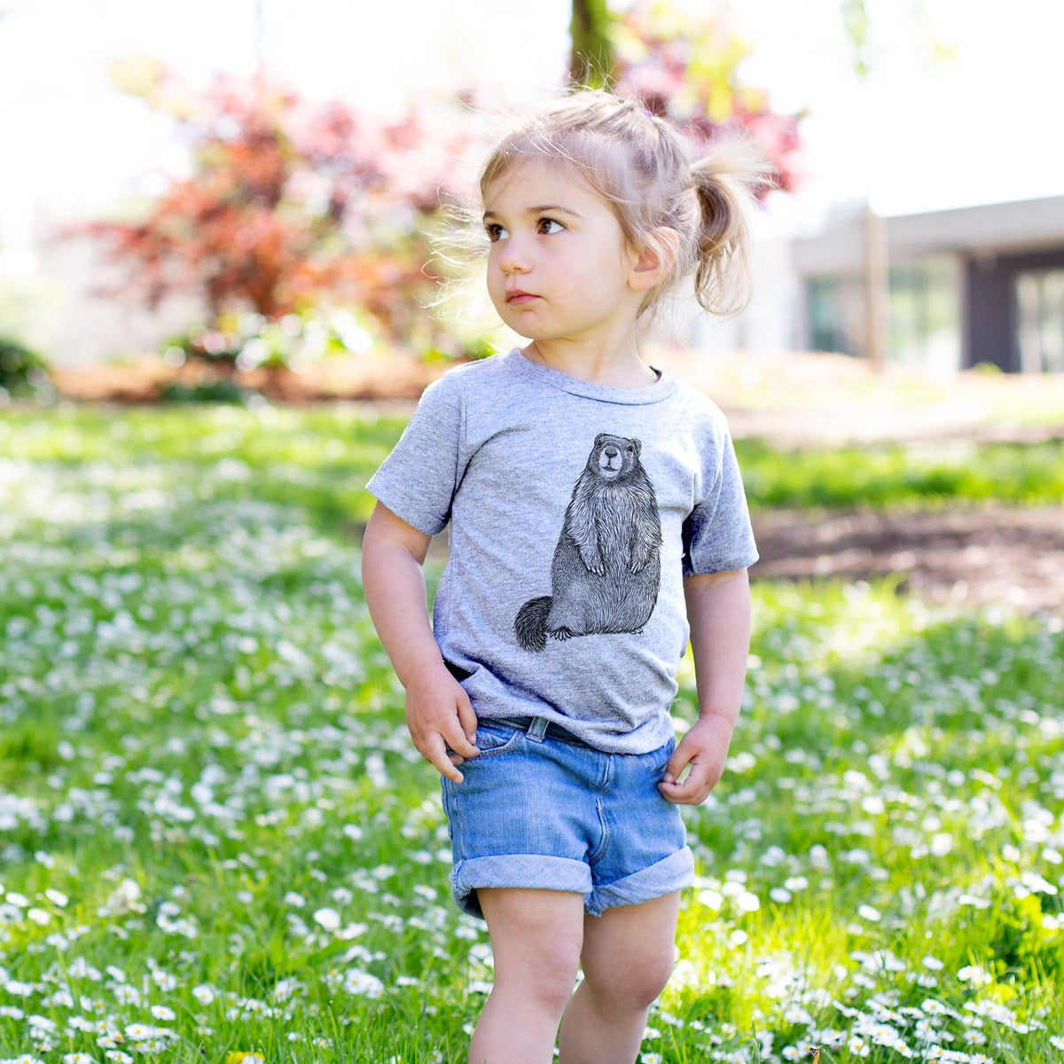 Toddler girl walking outdoors wearing a t-shirt printed with a detailed black ink illustration of a marmot standing upright.