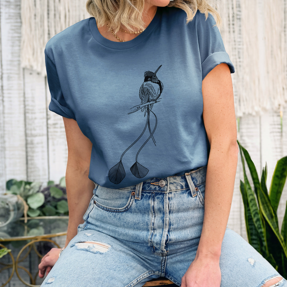 Woman wearing a steel blue lightweight cotton t-shirt printed with a black ink illustration of a marvelous spatuletail hummingbird perched, with its two long racket-tipped tail feathers.