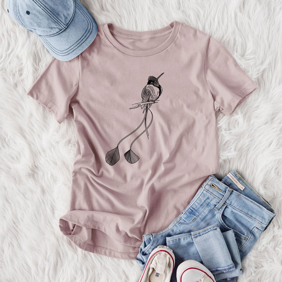 Women's relaxed fit cotton t-shirt printed with a black ink illustration of a marvelous spatuletail hummingbird perched, with its two long racket-tipped tail feathers, styled flat on a white faux fur rug with jeans.