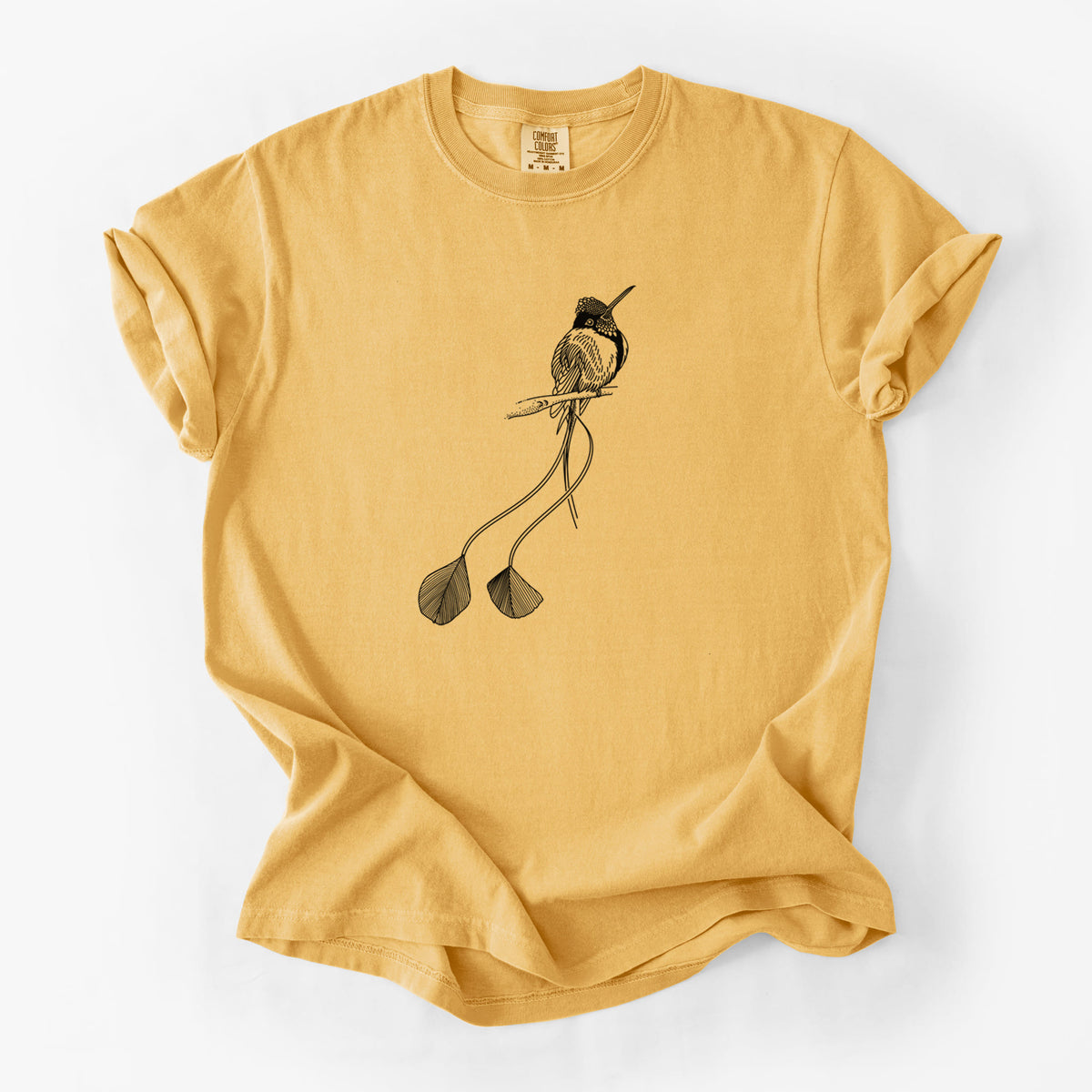 Golden wheat yellow Comfort Colors t-shirt laid flat, printed with a black ink illustration of a marvelous spatuletail hummingbird perched, with its two long racket-tipped tail feathers.