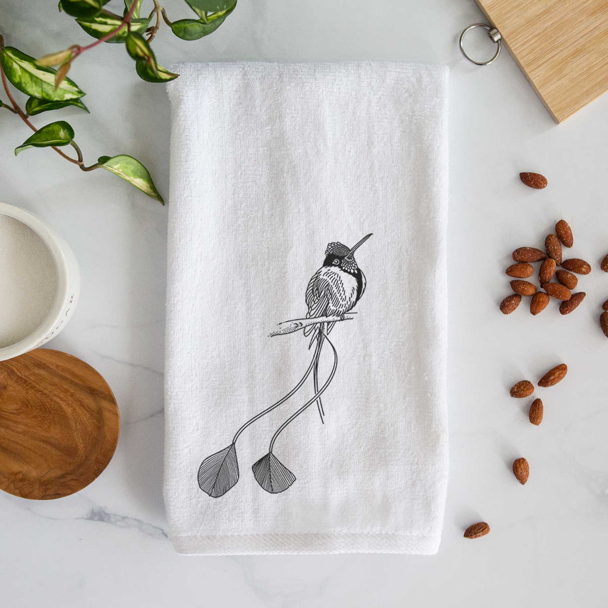 White hand towel printed with a black ink illustration of a marvelous spatuletail hummingbird perched, with its two long racket-tipped tail feathers.