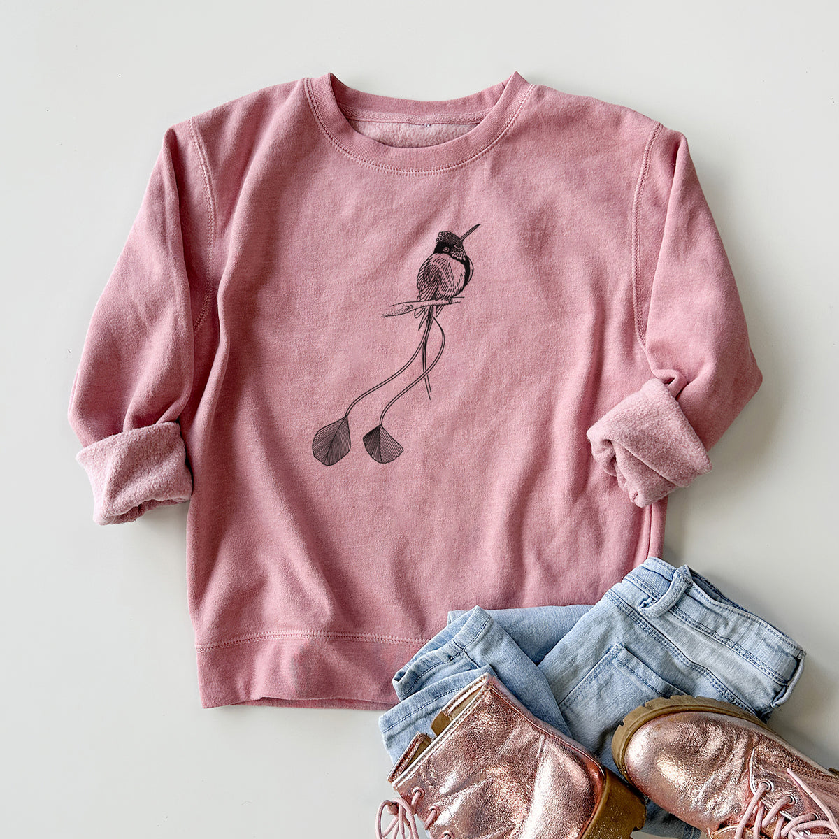 Youth crewneck sweatshirt printed with a black ink illustration of a marvelous spatuletail hummingbird perched, with its two long racket-tipped tail feathers, styled flat with jeans and boots.