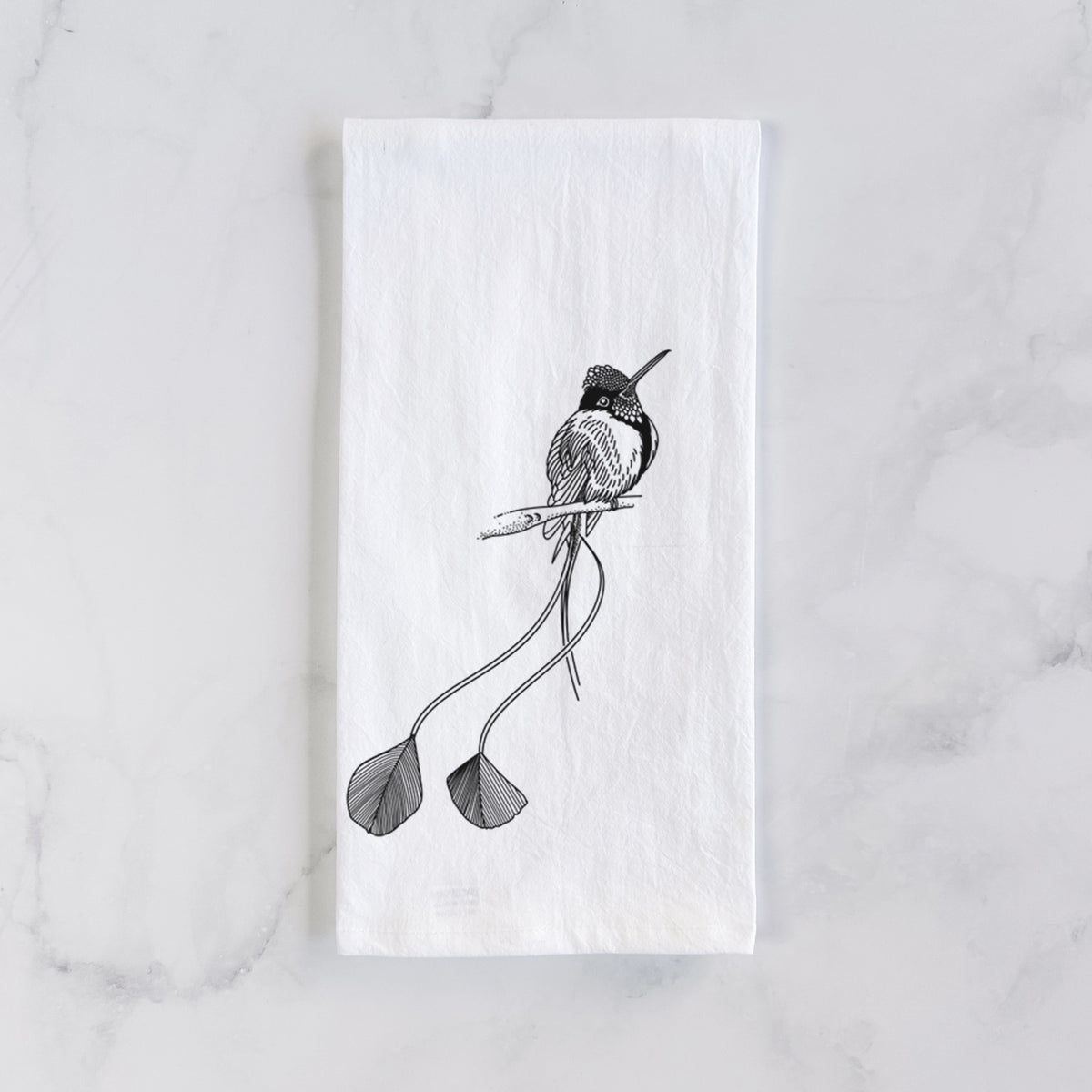 White cotton tea towel laid flat on marble, printed with a black ink illustration of a marvelous spatuletail hummingbird perched, with its two long racket-tipped tail feathers.