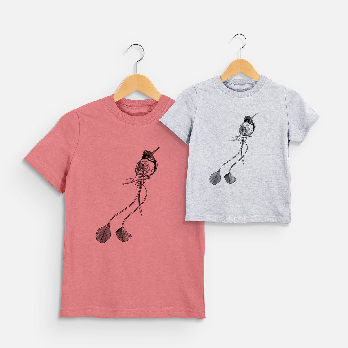 Two youth t-shirts in different colors on hangers, printed with a black ink illustration of a marvelous spatuletail hummingbird perched, with its two long racket-tipped tail feathers.