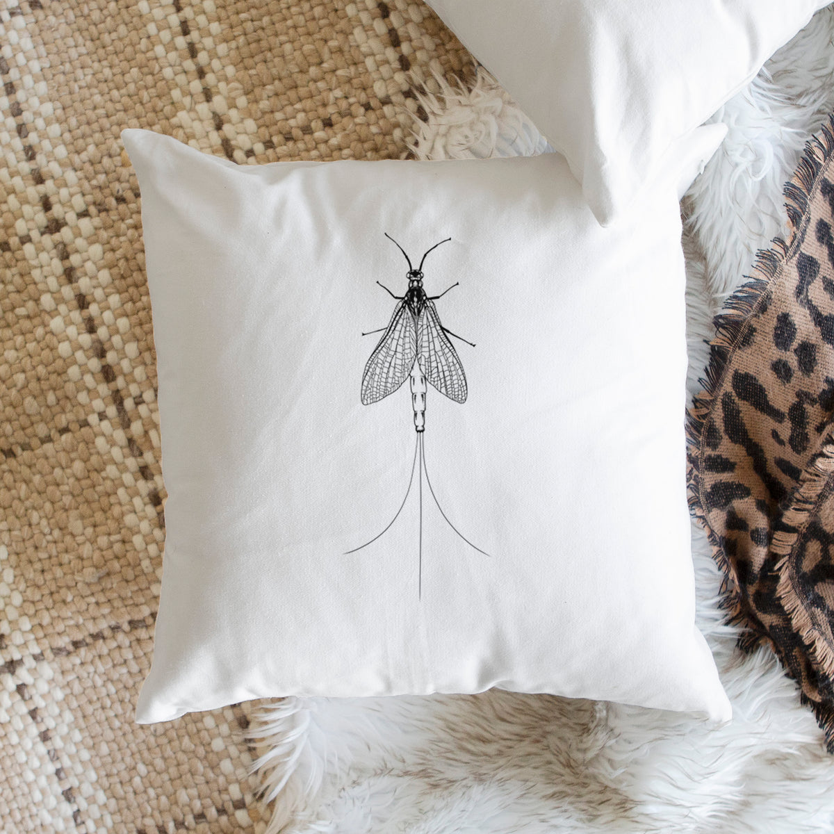 White pillow cover printed with a detailed black ink illustration of a mayfly with its wings raised and long tail filaments, on a woven chair.