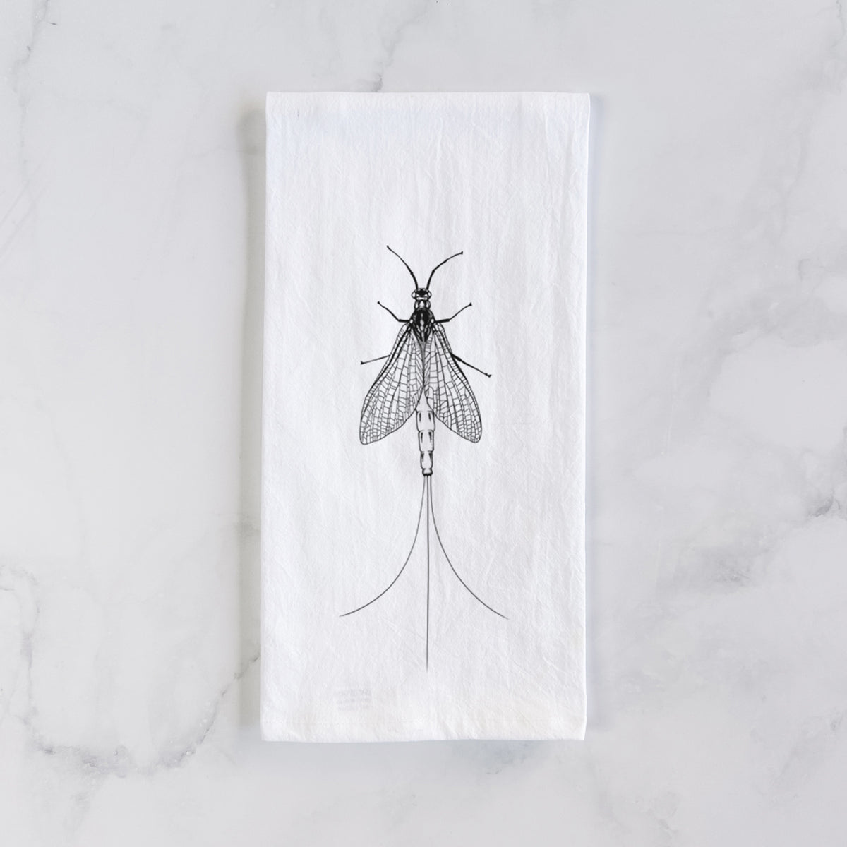 White cotton tea towel laid flat on marble, printed with a detailed black ink illustration of a mayfly with its wings raised and long tail filaments.