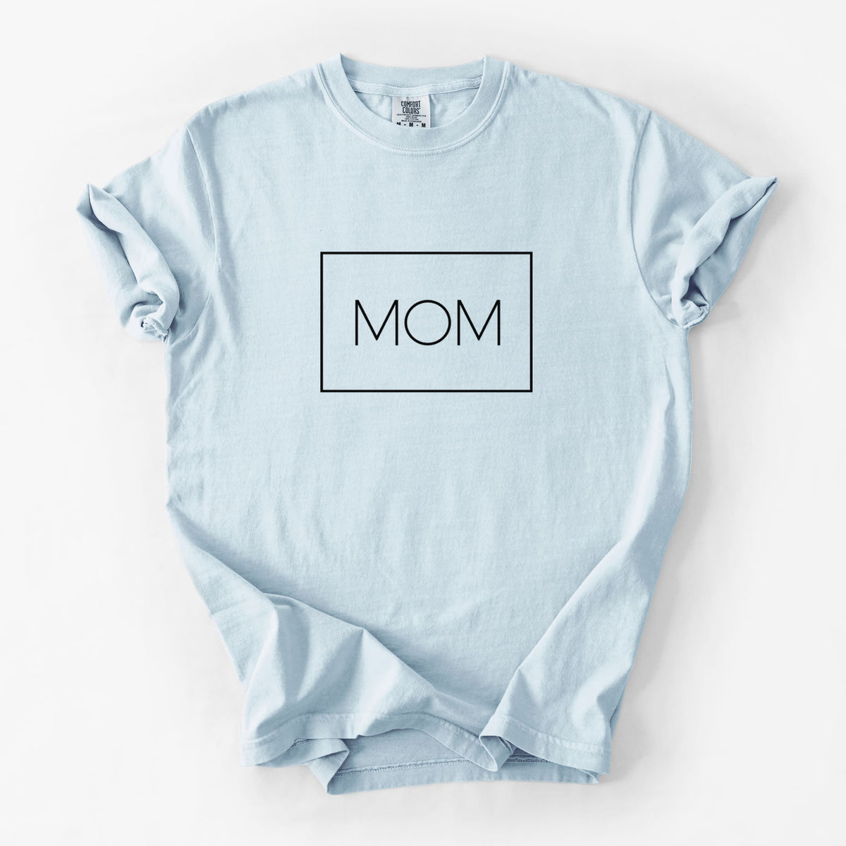 Chambray blue Comfort Colors t-shirt laid flat, printed with the word MOM in thin black letters inside a rectangle outline.
