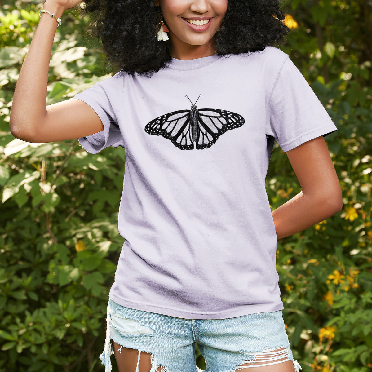 Woman wearing a Comfort Colors t-shirt printed with a detailed black ink illustration of a monarch butterfly with its wings spread, outdoors.
