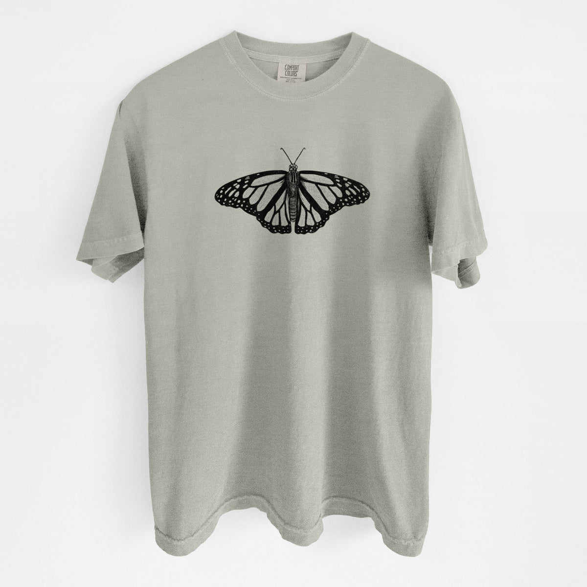 Sandstone beige Comfort Colors t-shirt laid flat, printed with a detailed black ink illustration of a monarch butterfly with its wings spread.