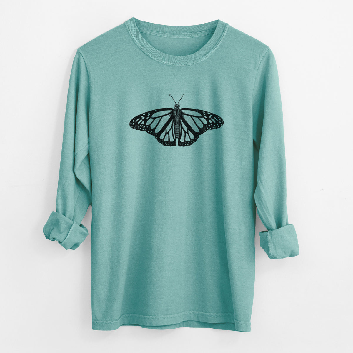 Reef green Comfort Colors long sleeve shirt laid flat with the cuffs rolled, printed with a detailed black ink illustration of a monarch butterfly with its wings spread.