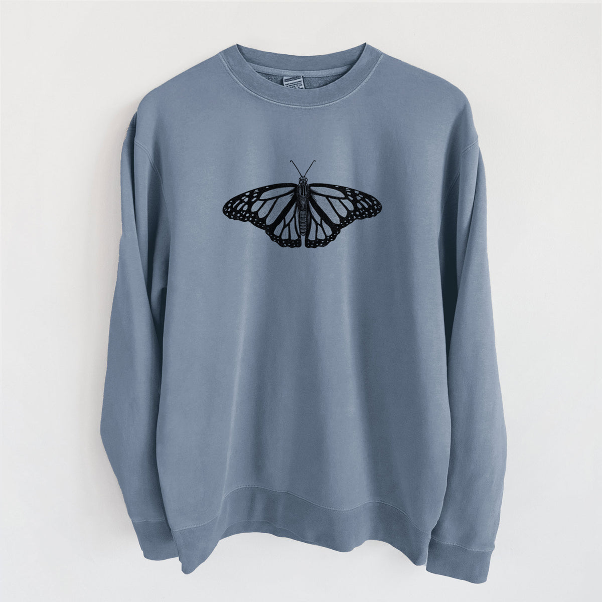 Slate blue pigment dyed crewneck sweatshirt laid flat, printed with a detailed black ink illustration of a monarch butterfly with its wings spread.
