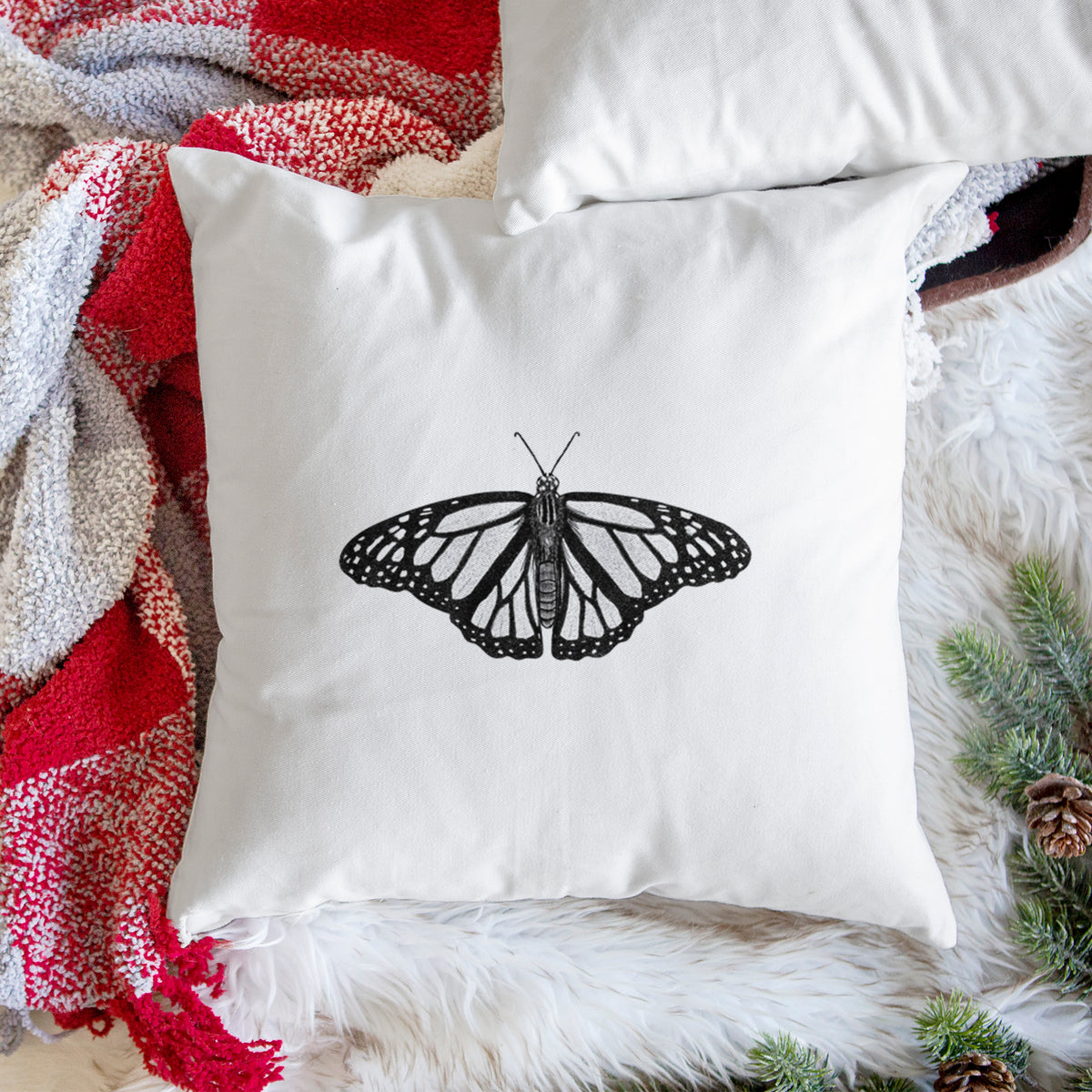 White pillow cover printed with a detailed black ink illustration of a monarch butterfly with its wings spread, on a woven chair.