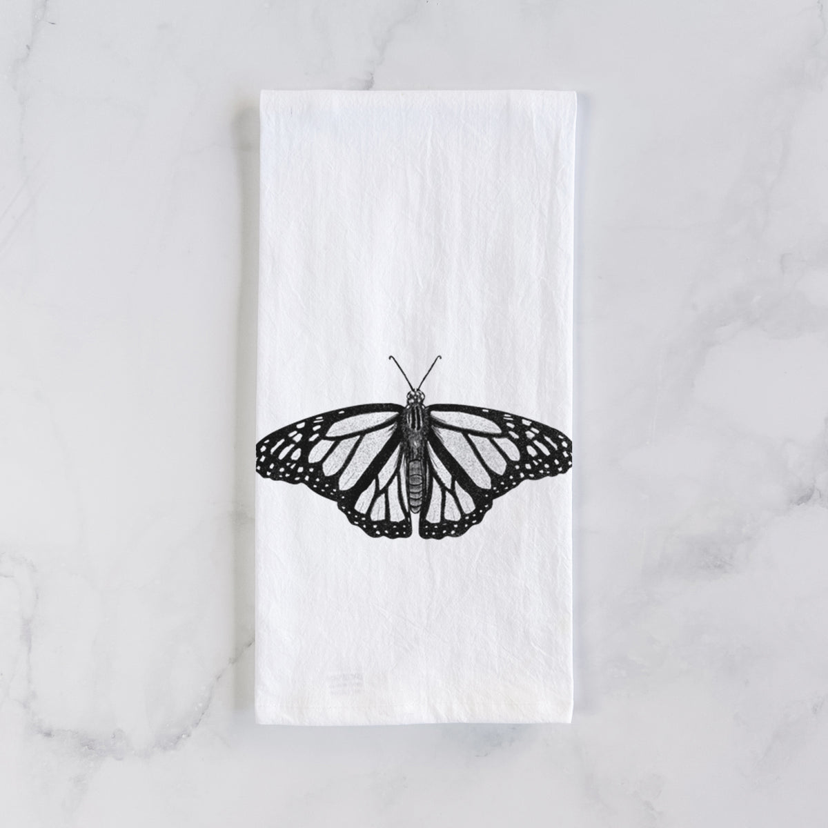 White cotton tea towel laid flat on marble, printed with a detailed black ink illustration of a monarch butterfly with its wings spread.