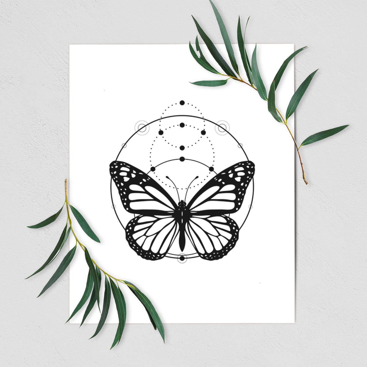 Art print of a black ink monarch butterfly inside a circle, beneath a line of moon phases, shown with eucalyptus leaves.