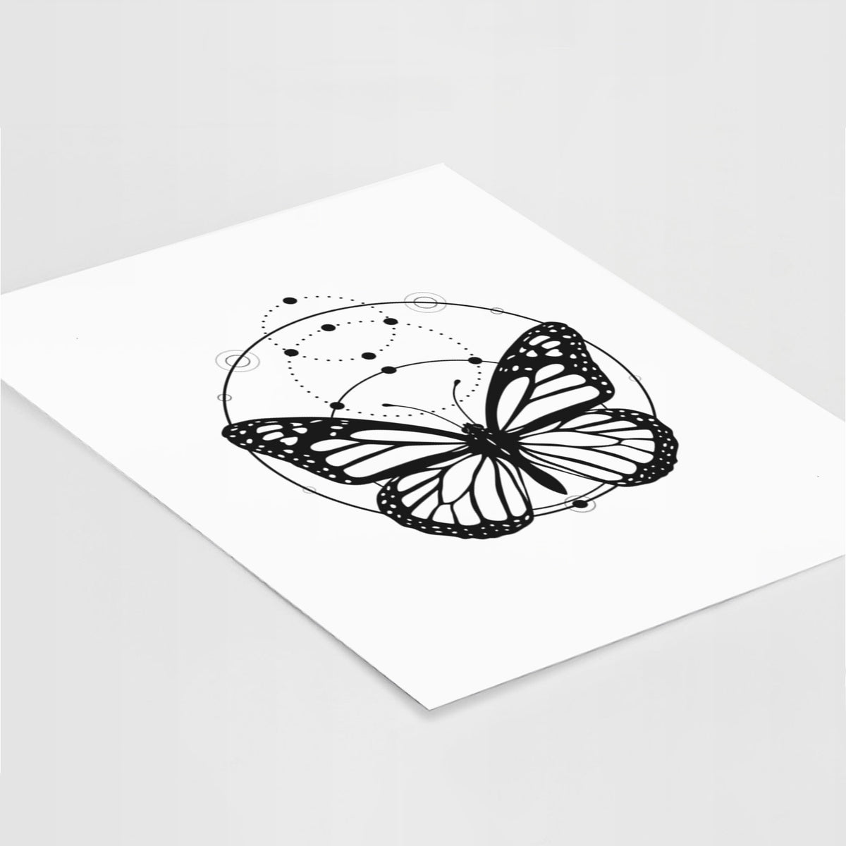 Art print of a black ink monarch butterfly inside a circle, beneath a line of moon phases, lying at an angle on a white surface.