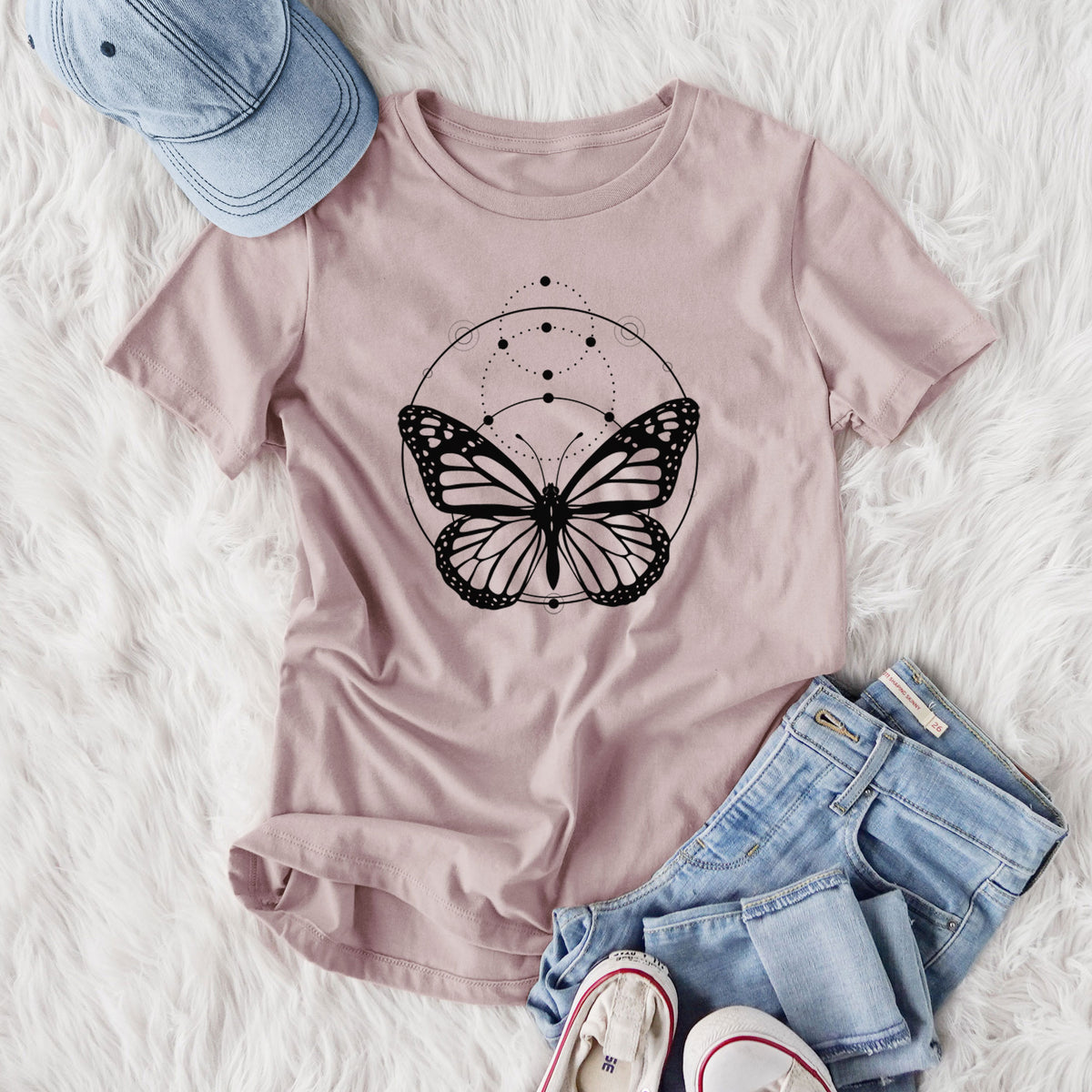 Women's relaxed fit cotton t-shirt printed with a black ink monarch butterfly inside a circle, beneath a line of moon phases, styled flat on a white faux fur rug with jeans.