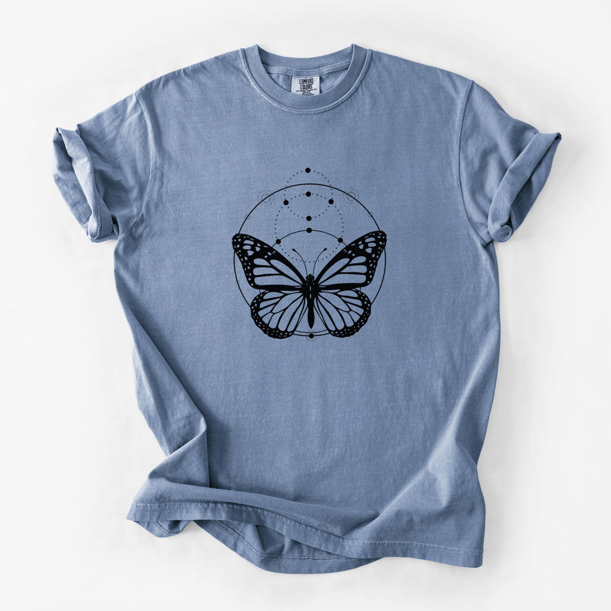 Blue jean Comfort Colors t-shirt laid flat, printed with a black ink monarch butterfly inside a circle, beneath a line of moon phases.