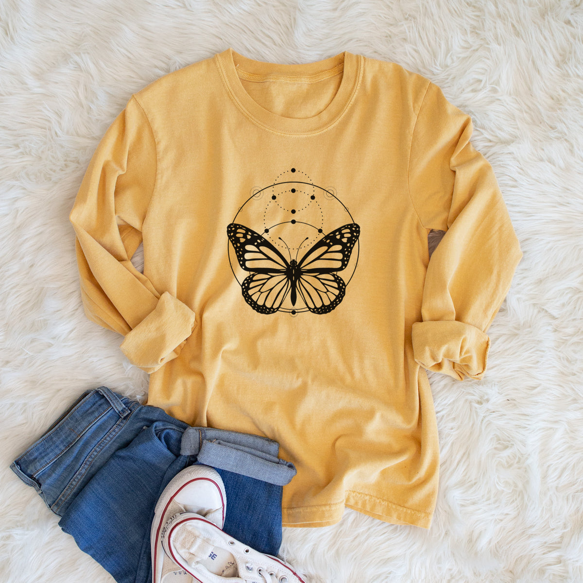 Golden wheat yellow Comfort Colors long sleeve shirt printed with a black ink monarch butterfly inside a circle, beneath a line of moon phases, shown in a lifestyle photo.