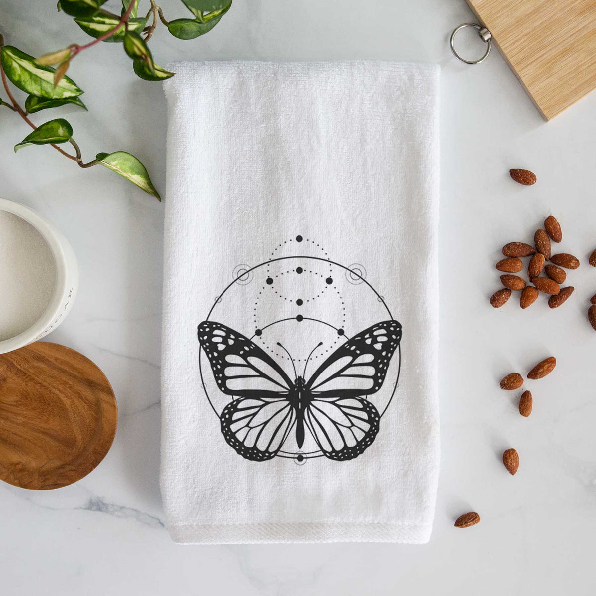 White hand towel printed with a black ink monarch butterfly inside a circle, beneath a line of moon phases.