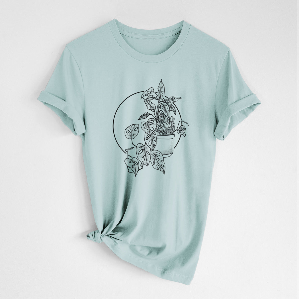 Dusty blue lightweight cotton t-shirt laid flat with the sleeves rolled, printed with a black ink illustration of a potted Monsteradansonii plant with trailing vines in front of a circle.