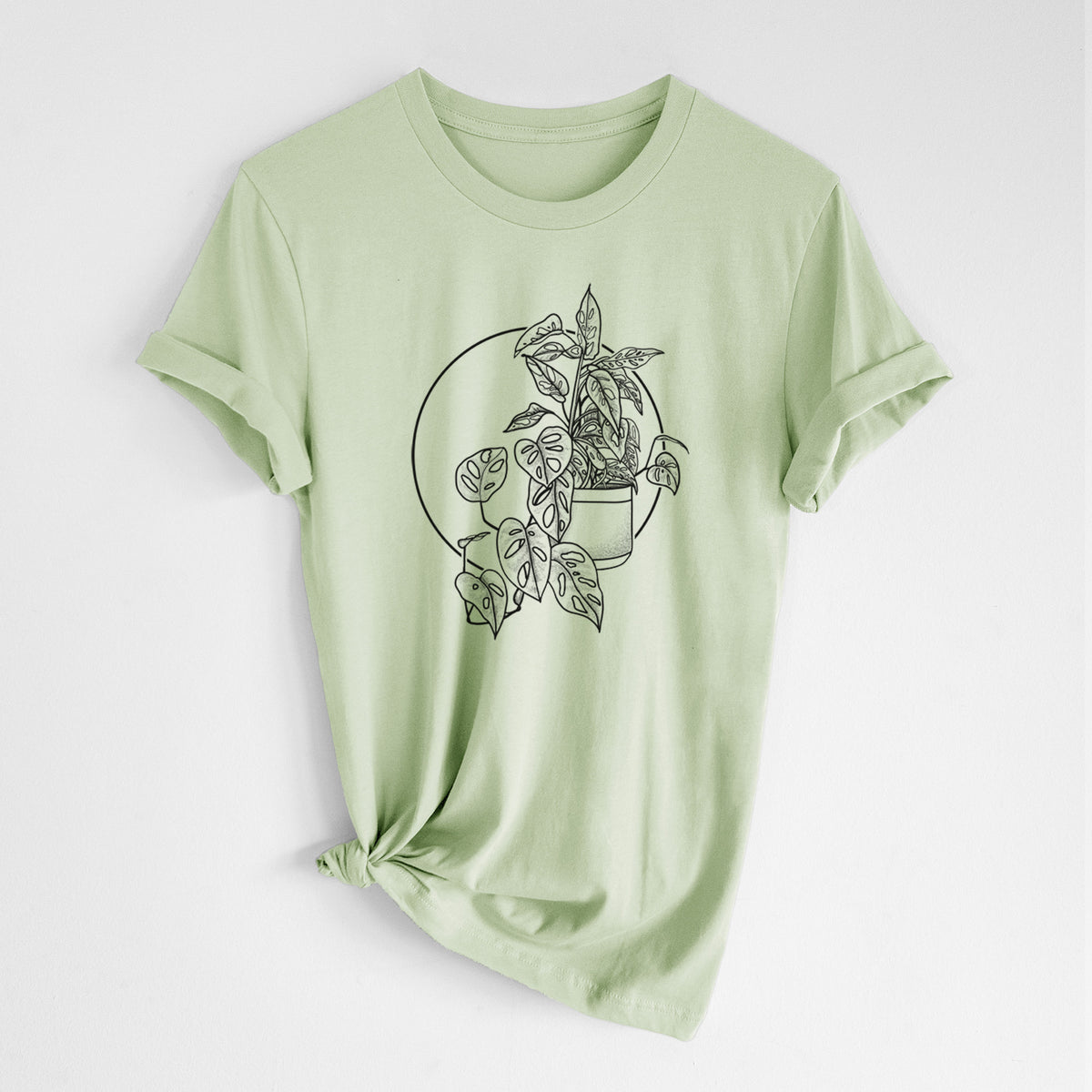 Spring green lightweight cotton t-shirt laid flat with the sleeves rolled, printed with a black ink illustration of a potted Monsteradansonii plant with trailing vines in front of a circle.