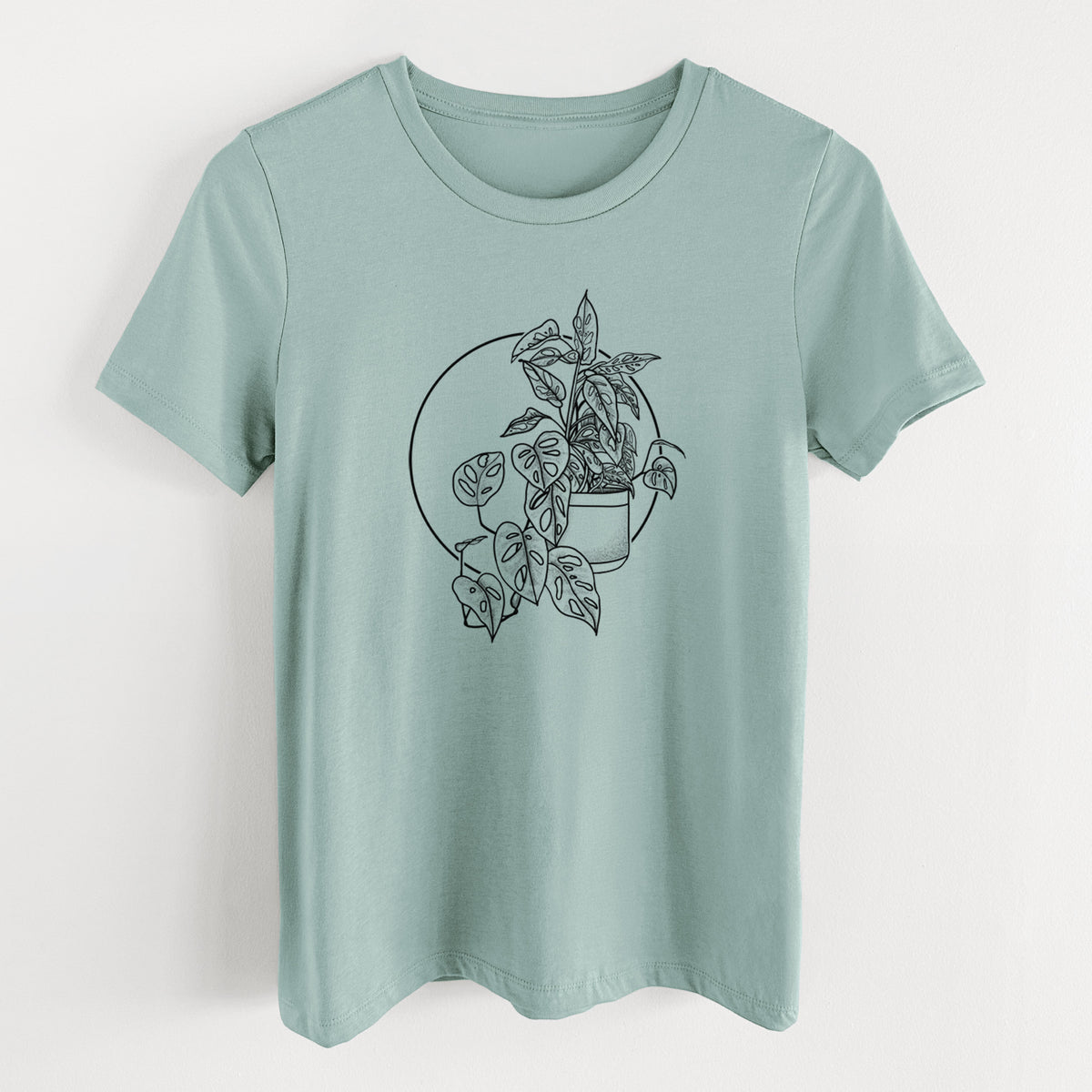 Dusty blue women's relaxed fit cotton t-shirt laid flat, printed with a black ink illustration of a potted Monsteradansonii plant with trailing vines in front of a circle.