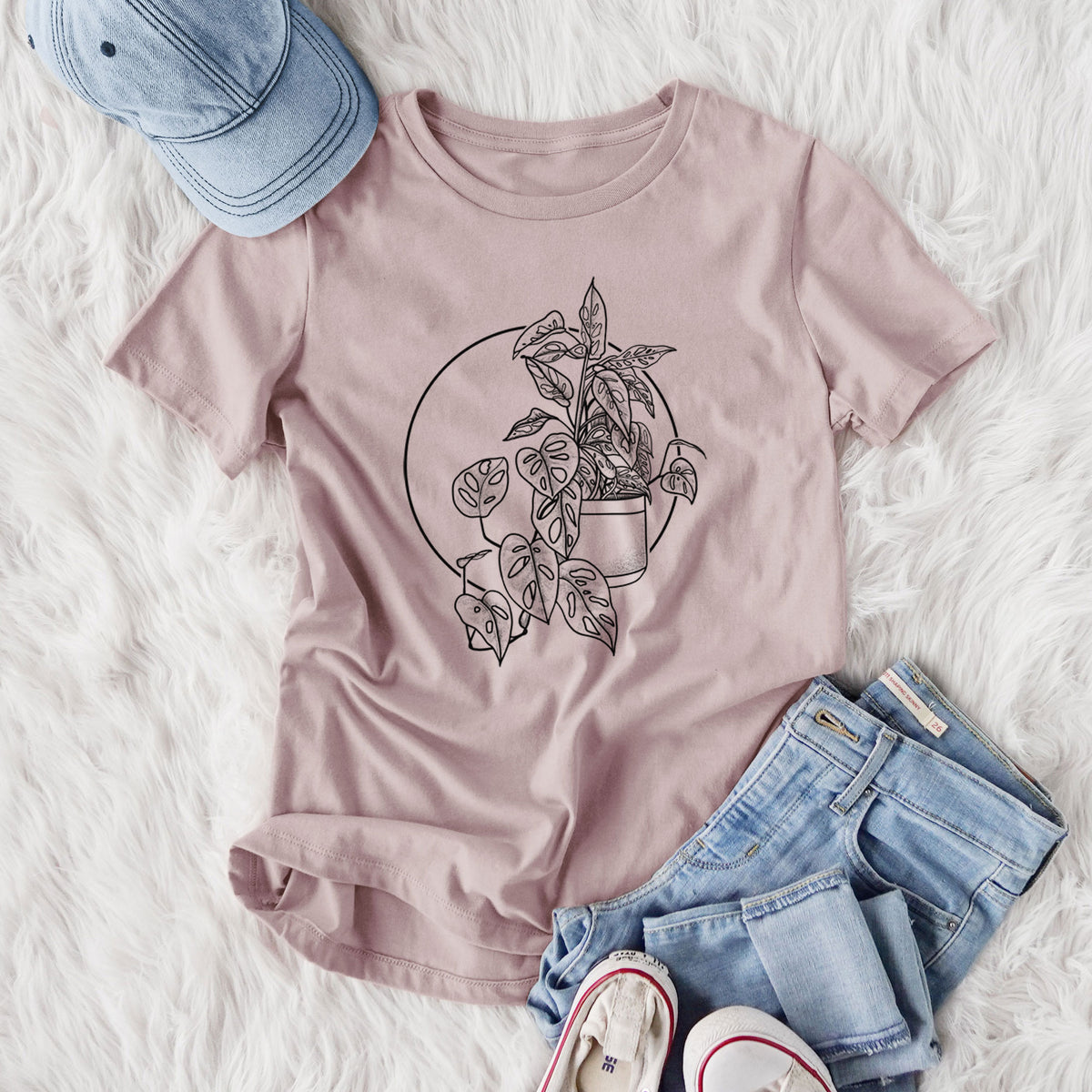 Women's relaxed fit cotton t-shirt printed with a black ink illustration of a potted Monsteradansonii plant with trailing vines in front of a circle, styled flat on a white faux fur rug with jeans.