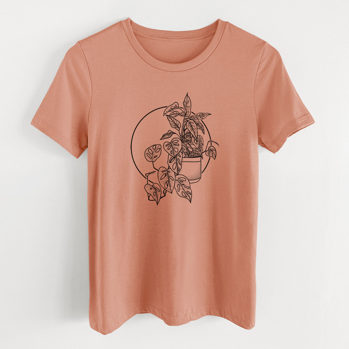 Terracotta orange women's relaxed fit cotton t-shirt laid flat, printed with a black ink illustration of a potted Monsteradansonii plant with trailing vines in front of a circle.
