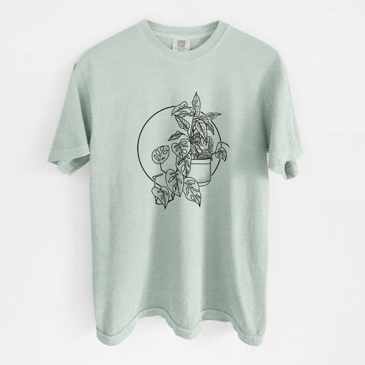 Bay green Comfort Colors t-shirt laid flat, printed with a black ink illustration of a potted Monsteradansonii plant with trailing vines in front of a circle.