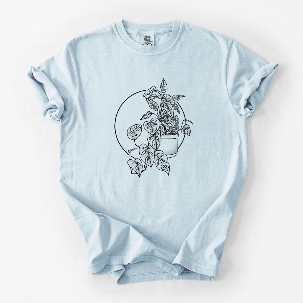 Chambray blue Comfort Colors t-shirt laid flat, printed with a black ink illustration of a potted Monsteradansonii plant with trailing vines in front of a circle.