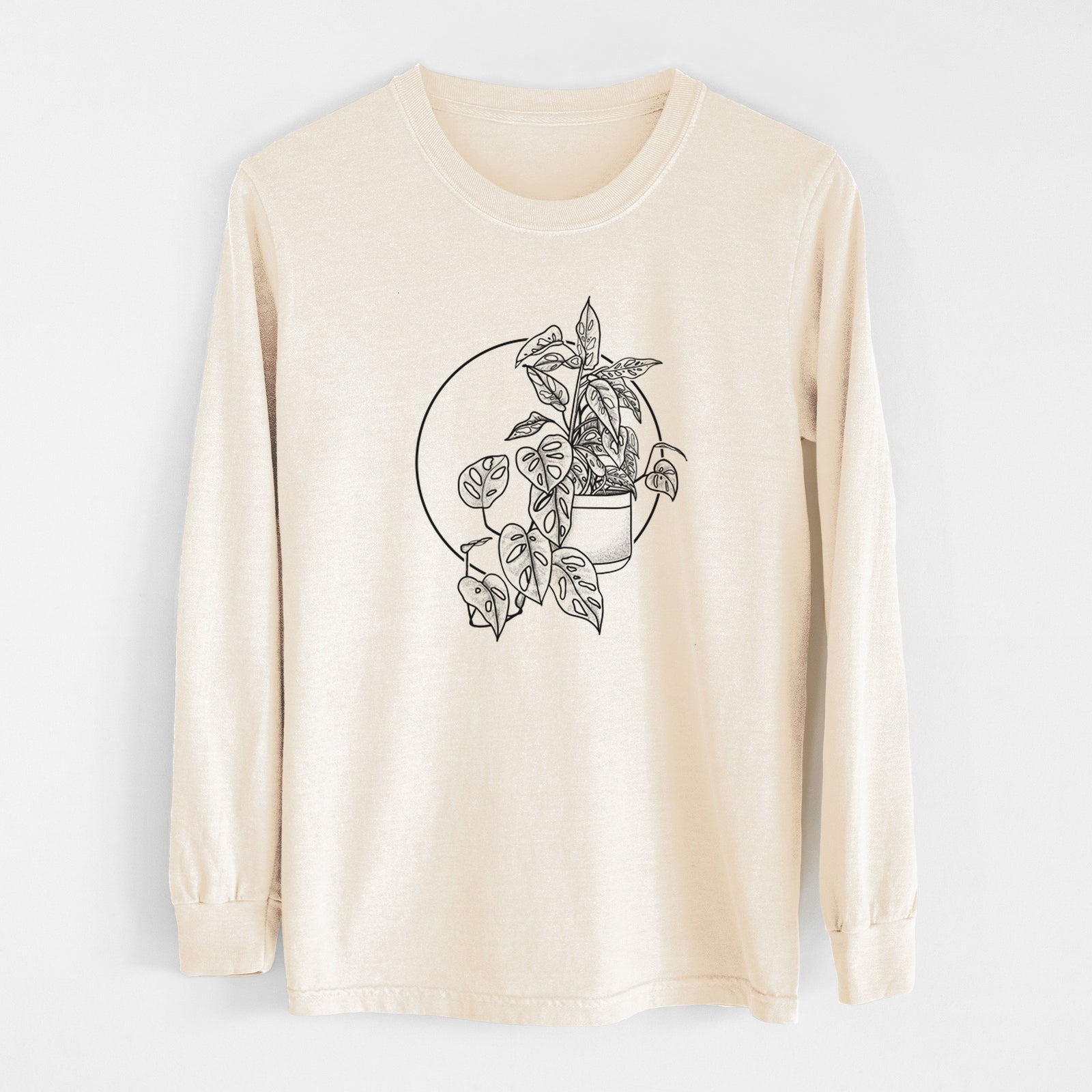 Ivory Comfort Colors long sleeve shirt laid flat, printed with a black ink illustration of a potted Monsteradansonii plant with trailing vines in front of a circle.