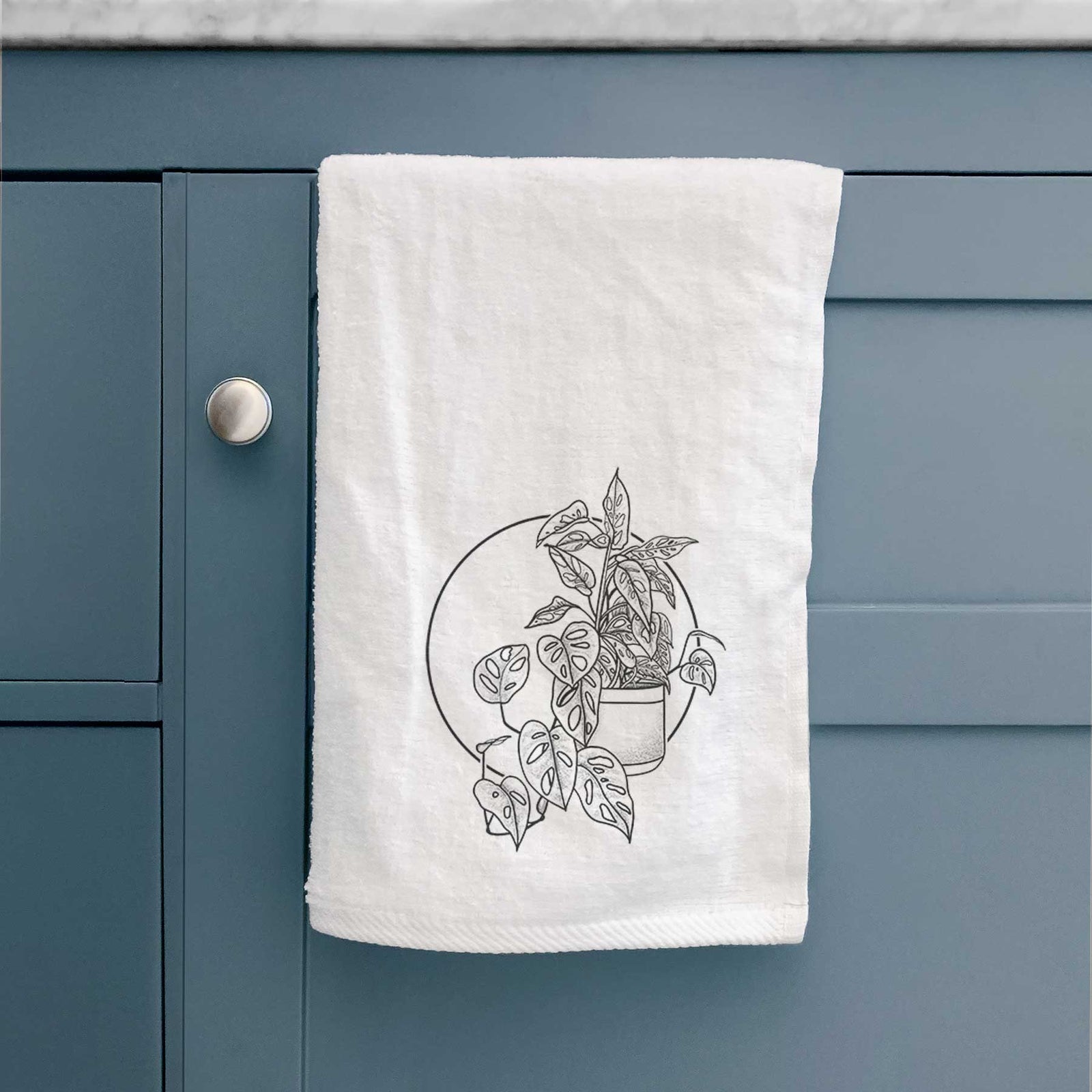 White hand towel printed with a black ink illustration of a potted Monsteradansonii plant with trailing vines in front of a circle.