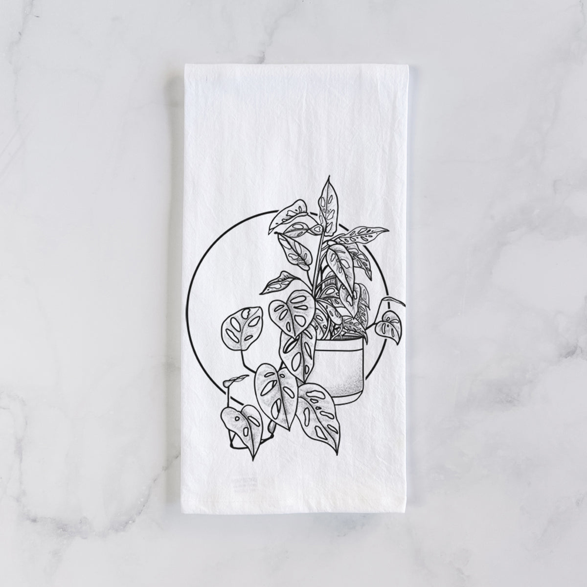 White cotton tea towel laid flat on marble, printed with a black ink illustration of a potted Monsteradansonii plant with trailing vines in front of a circle.