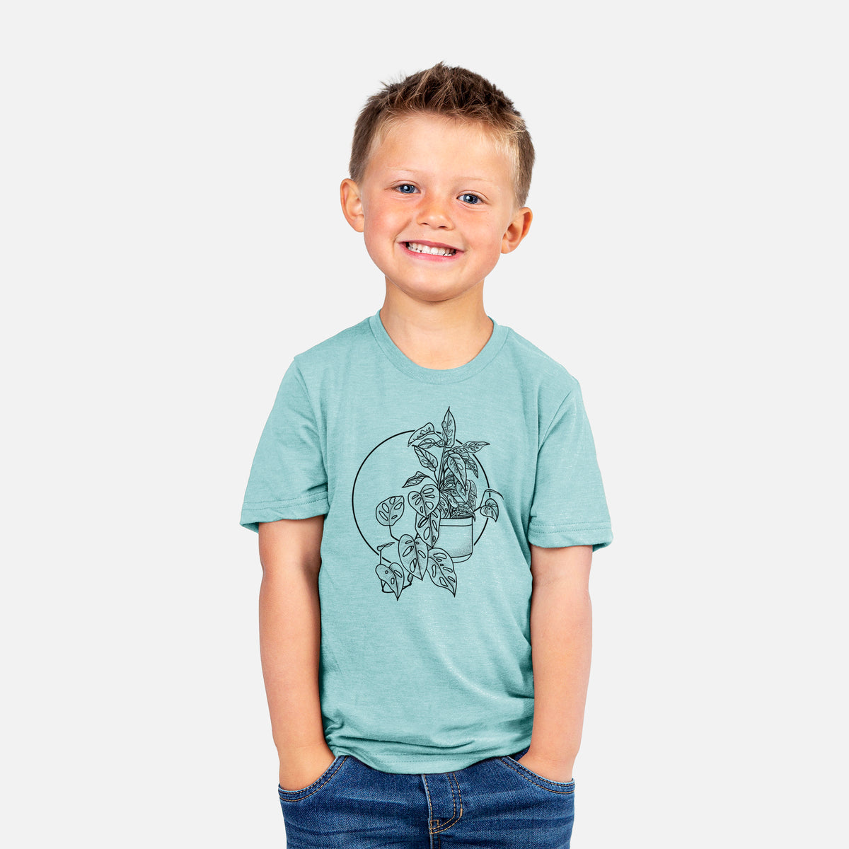 Smiling boy wearing a youth t-shirt printed with a black ink illustration of a potted Monsteradansonii plant with trailing vines in front of a circle.