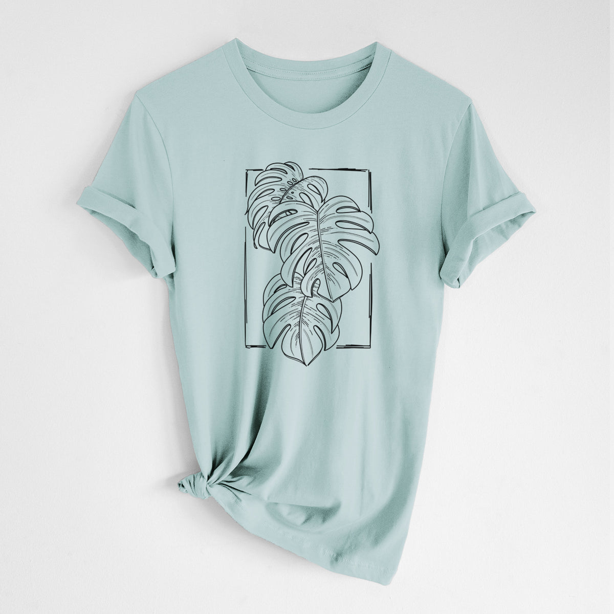 Dusty blue lightweight cotton t-shirt laid flat with the sleeves rolled, printed with a black ink line drawing of Monstera deliciosa leaves inside a rectangle outline.