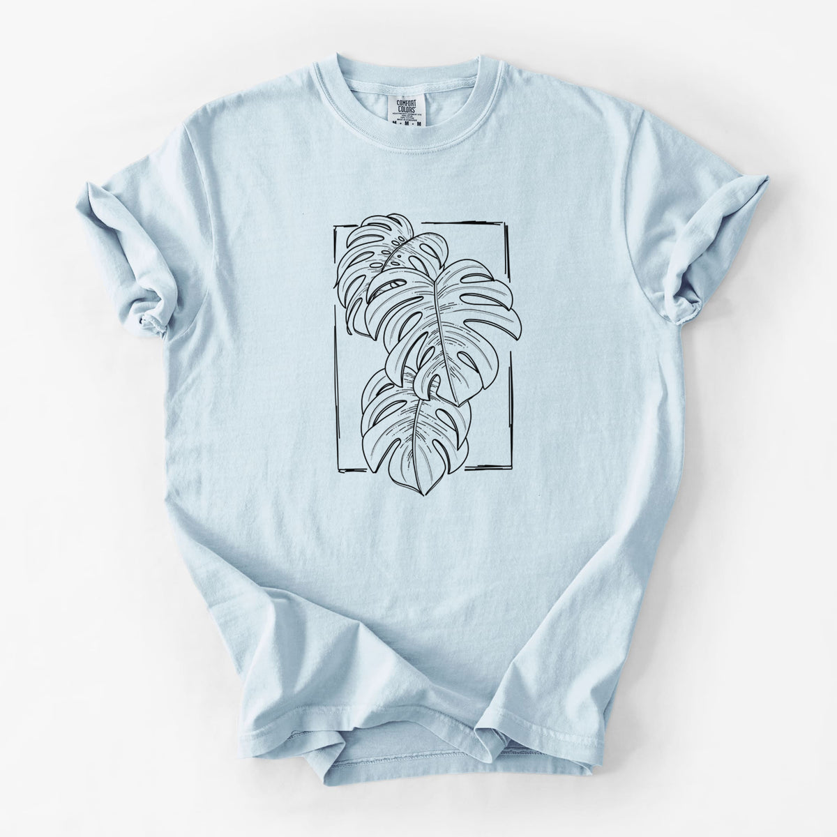 Chambray blue Comfort Colors t-shirt laid flat, printed with a black ink line drawing of Monstera deliciosa leaves inside a rectangle outline.