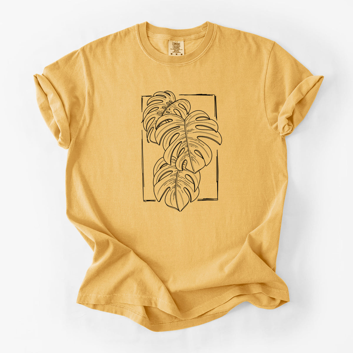 Golden wheat yellow Comfort Colors t-shirt laid flat, printed with a black ink line drawing of Monstera deliciosa leaves inside a rectangle outline.