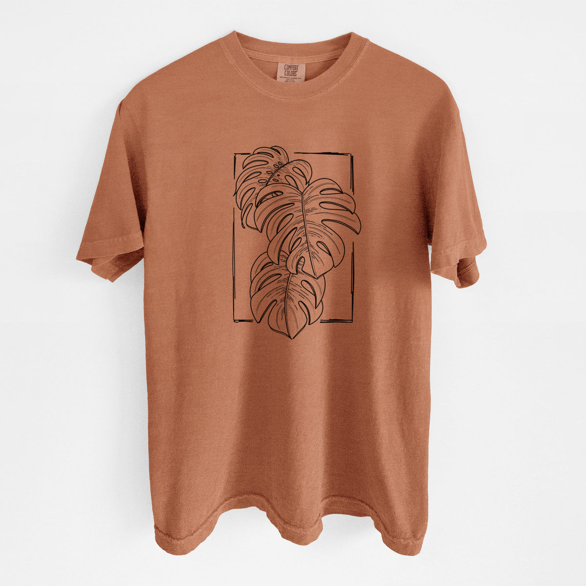 Yam burnt orange Comfort Colors t-shirt laid flat, printed with a black ink line drawing of Monstera deliciosa leaves inside a rectangle outline.